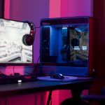 a gaming setup with a PC, monitor, headset, keyboard and mouse, a chair sits next to the desk. Purple lighting in various shades is in the background