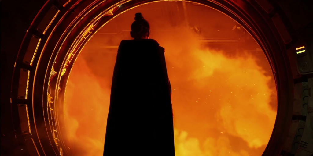 A robed woman stands in what looks to be a ship door entryway surroundd by orange coloring and black smoke